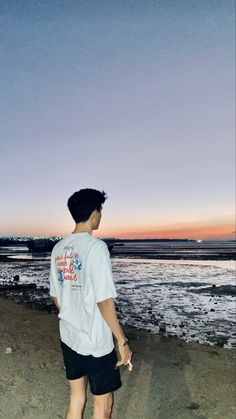 a man standing on top of a sandy beach next to the ocean at sunset or dawn