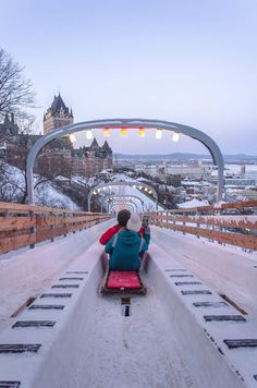 a person sitting in a sled on top of a snow covered slope next to a city