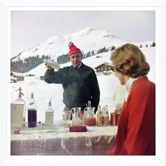 a man and woman sitting at a table in front of a mountain with liquor bottles on it