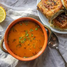 a bowl of soup next to a plate with bread and lemon wedges on it