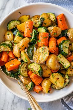 a white bowl filled with roasted vegetables on top of a marble counter next to a fork