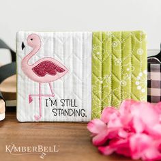 a pink flamingo sitting on top of a wooden table next to a vase with flowers