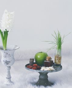 two vases with flowers, an apple and other items on a white fur surface