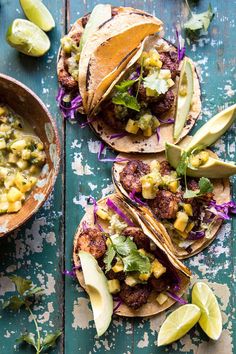 three tacos with meat, corn and avocado salsa on them sitting on a wooden table