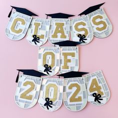 graduation decorations with gold glitter letters and black caps hanging from the side on a pink background