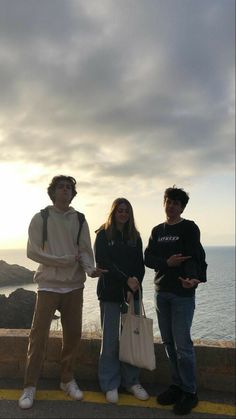 three people standing next to each other on the side of a road near the ocean