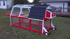 a red and white chicken coop sitting on top of a grass covered field next to a house