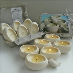 there are many white candles in bowls and one has a small bird on the side