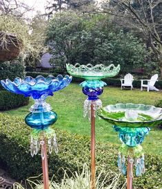 three glass dishes sitting on top of metal poles in front of some bushes and trees