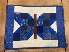 a blue and white quilted table runner with a cross on the center, in front of a wooden floor