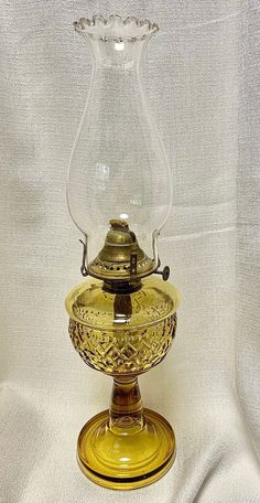 an old fashioned glass and brass oil lamp on a white cloth covered tablecloth,