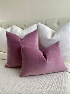 two purple and white pillows sitting on top of a bed next to eachother