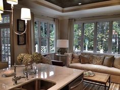 a living room filled with lots of furniture next to a kitchen sink and window covered in curtains