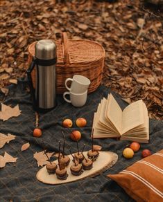 an open book, cupcakes and apples are on a blanket in the woods