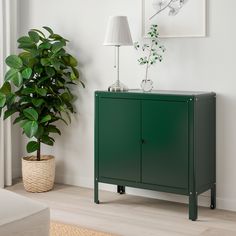 a green cabinet next to a potted plant in a living room with white walls