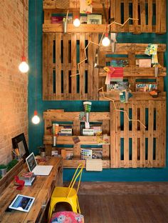 a room with wooden pallets on the wall and desks in front of it