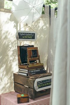 an old fashioned camera sitting on top of some books under an umbrella in the shade