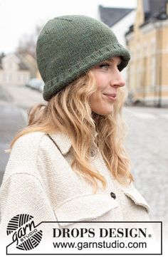 a woman wearing a green knitted hat and coat standing in front of a building