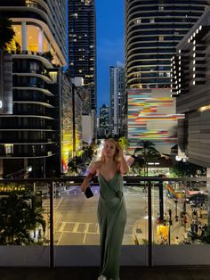 a woman in a green dress is standing on a balcony overlooking the city at night