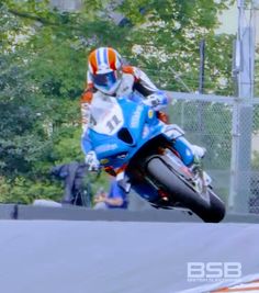 a man riding on the back of a blue motorcycle down a race track with trees in the background