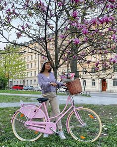 a woman standing next to a pink bike in front of a tree with purple flowers