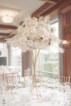 a tall vase filled with white flowers sitting on top of a table covered in wine glasses