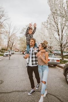 a man and woman walking down the street with their child on their shoulders while another person is riding a bike behind them