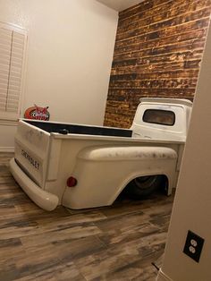 an old white truck is parked in the corner of a room with wood paneling on the walls