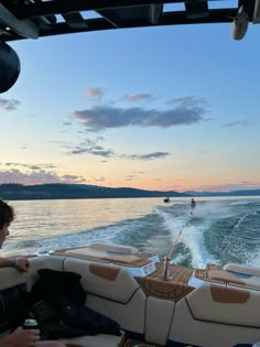 two people are riding on a boat in the water at sunset or dawn, while another person is skiing behind them