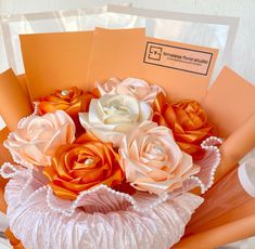 an orange and white flower arrangement in a vase with some papers on the table next to it