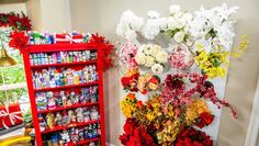 a red book shelf filled with flowers next to a wall hanging on the side of a room