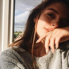 a woman with her hand on her chin leaning against the window sill looking at the camera