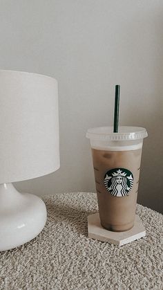 a starbucks drink sitting on top of a table next to a white lamp and shade