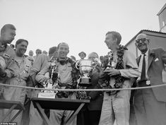 an old black and white photo of some men holding trophies in front of a group of people