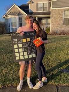 a man and woman standing in front of a house holding up a board with symbols on it