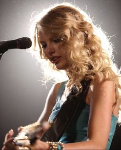 a woman with long blonde hair holding a guitar in front of a microphone on stage