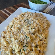 a white plate topped with macaroni and cheese next to a bowl of peas