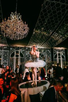 a ballerina is standing on top of a table in the middle of a room full of people