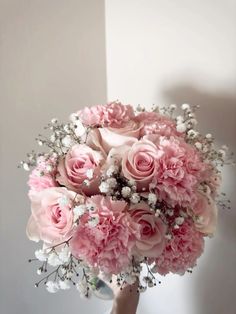 a bouquet of pink roses and baby's breath is held in front of a white wall