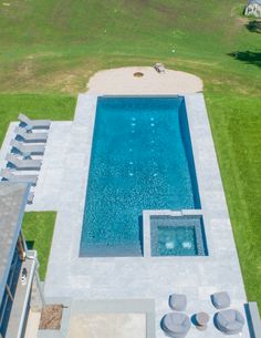 an aerial view of a swimming pool in the middle of a lawn with lounge chairs around it