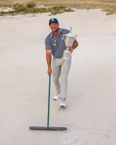 a man holding a trophy while standing on top of a sandy beach next to a golf ball