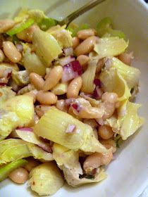 a white bowl filled with lettuce and beans next to a fork on top of a table