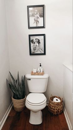 a white toilet sitting in a bathroom next to a plant and pictures on the wall