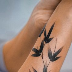 a woman's legs with black leaves tattoo on her arm and leg, while she is sitting down