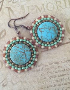 two pairs of turquoise and brown earrings on top of a piece of paper with writing in the background