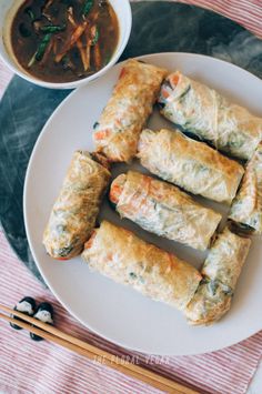 several rolls on a plate with dipping sauce and chopsticks next to the dish