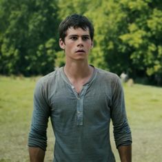 a young man standing in the middle of a field with trees in the back ground