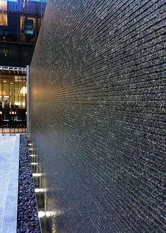 a water fountain in front of a tall building at night with lights shining on it