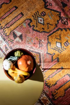 a bowl filled with fruits and vegetables on top of a colorful rug next to a table