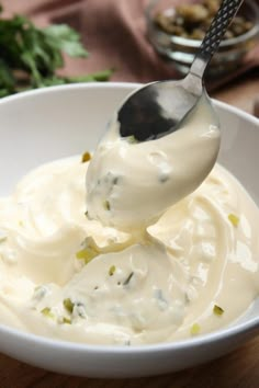 a spoon full of yogurt sitting in a white bowl on top of a wooden table